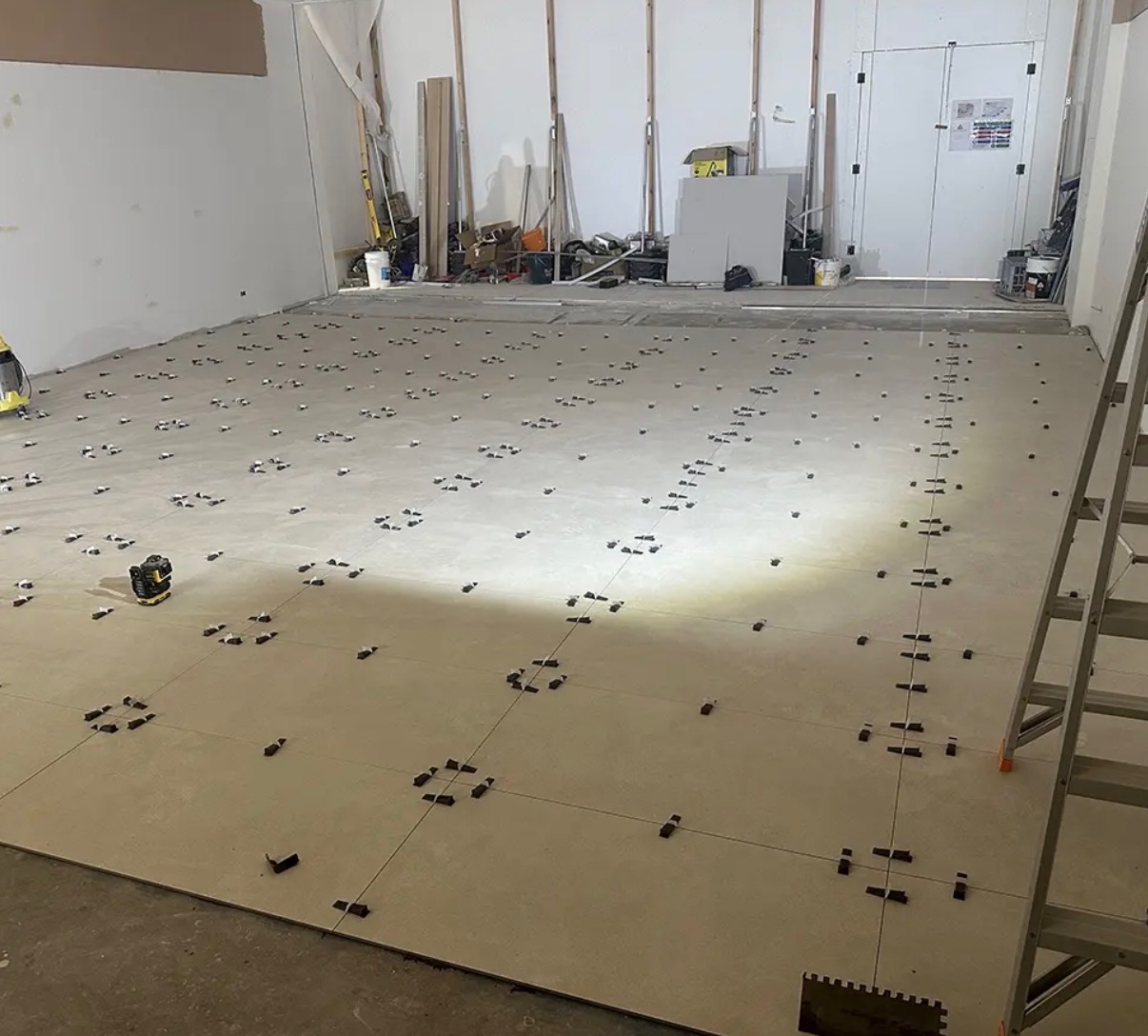 Large-format floor tiles being laid across an empty commercial space, with levelling clips in every joint