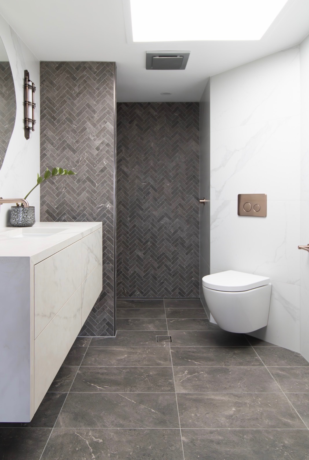 Bathroom with a dark herringbone mosaic feature wall, large-format dark stone-look floor tiles, white marble-look walls and a floating vanity