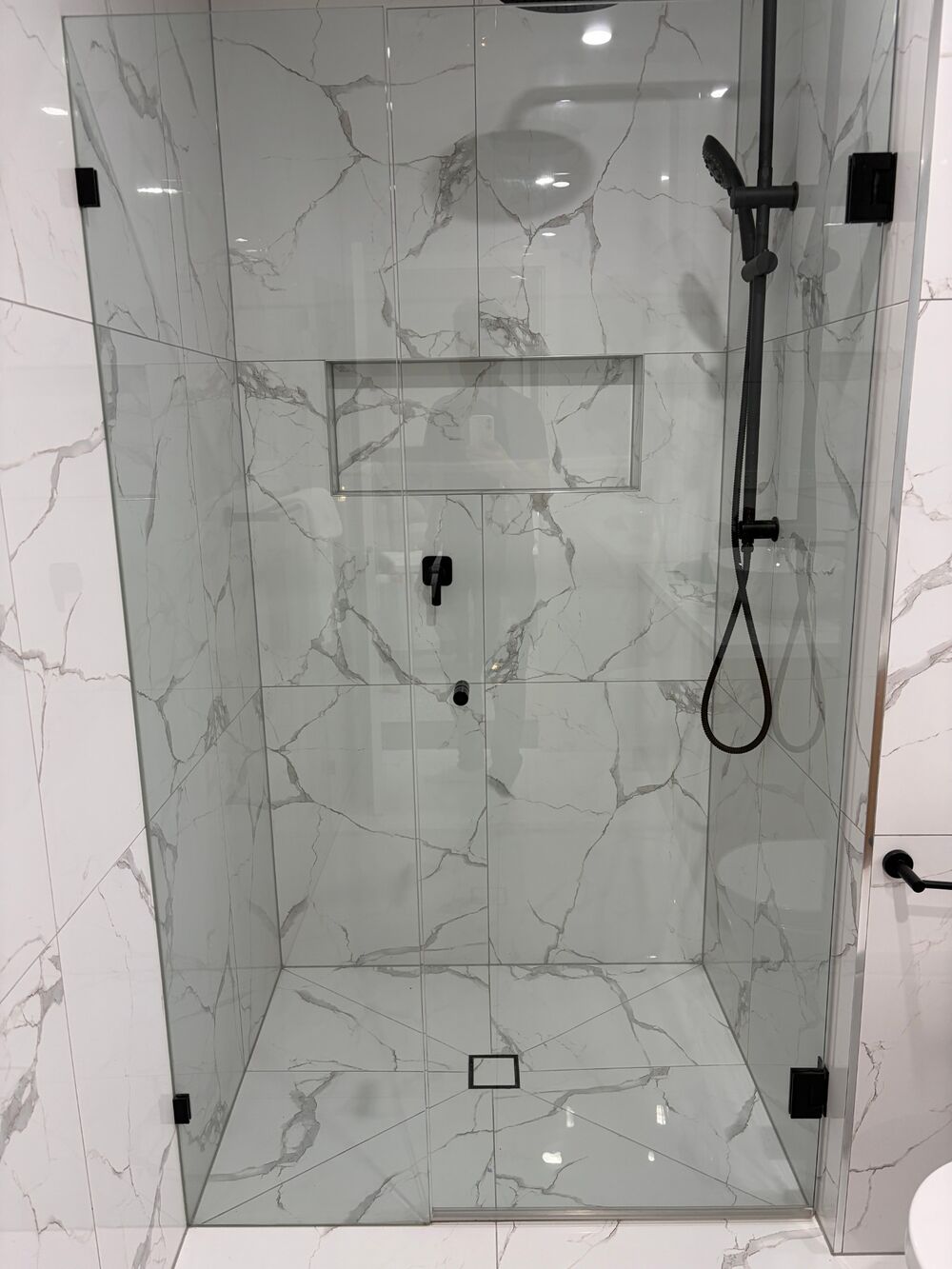 Walk-in shower with white marble-look tiles, a tiled niche and a tile-insert floor waste